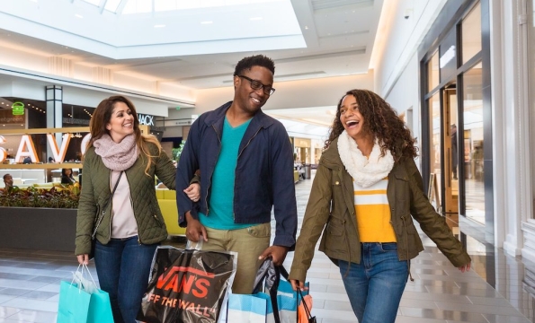 three people walking through shopping mall holding shopping bags and smiling