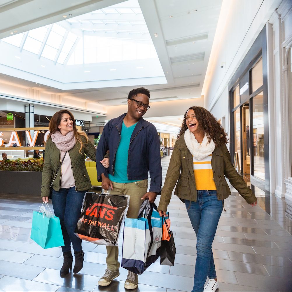 three people walking through shopping mall holding shopping bags and smiling