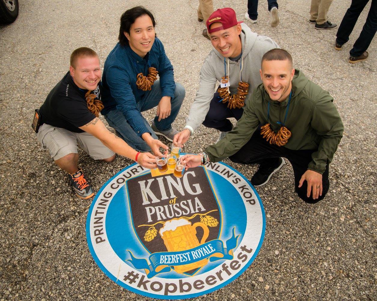 four people croucine around a circular decal on pavement, holding small beer mugs in the center
