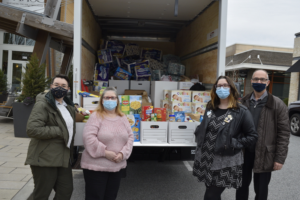 four people standing in front of an open box truck with a large amount of boxes inside
