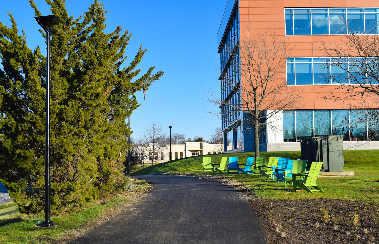outdoor view with a pathway, trees, light posts, colorful chairs and a red brick building