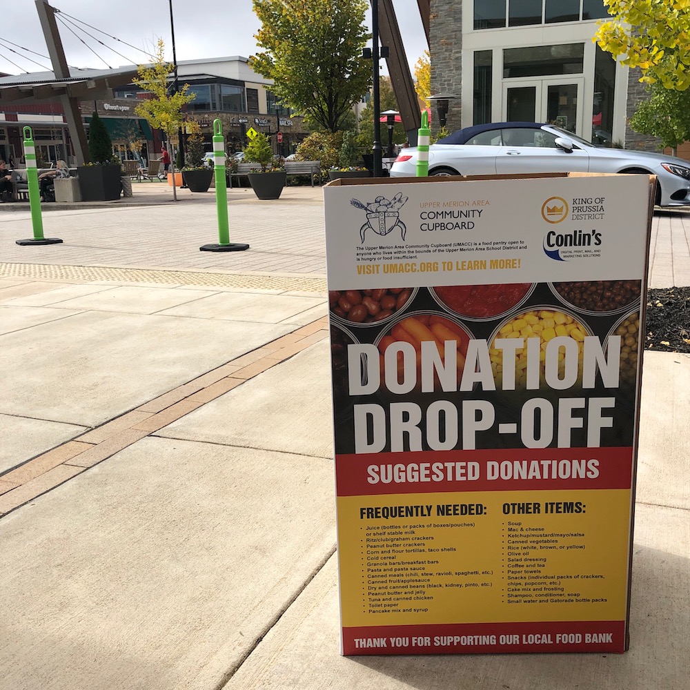 a large "donation drop-off: box outdoors on a sidewalk with.a road and car and buildings in the background