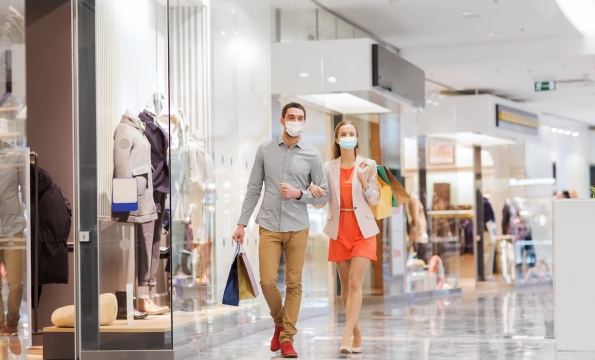 Man and woman walking arm in arm in shopping mall wearing masks
