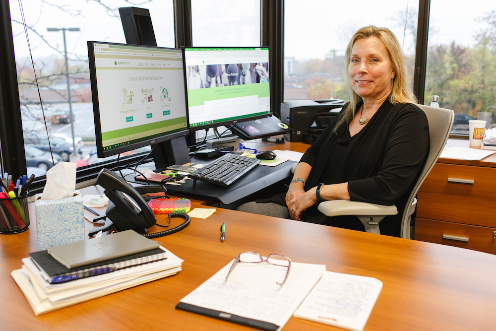 person sitting at desk in front of two monitors looking at the camera and smiling