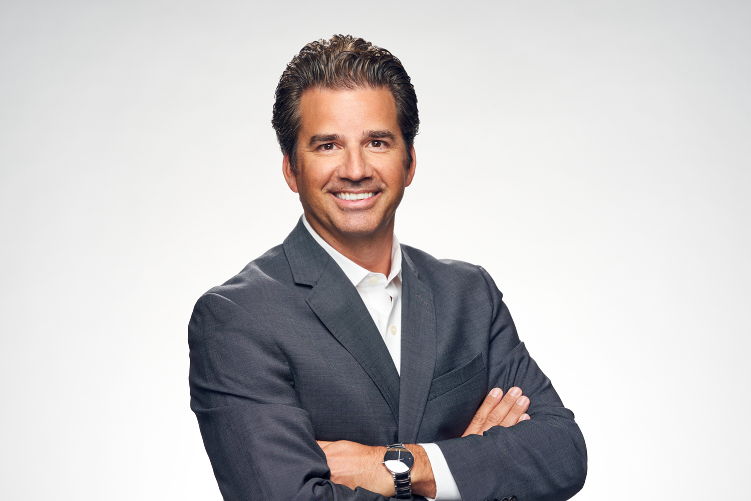 Person standing against white background in a blazer crossing their arms and smiling