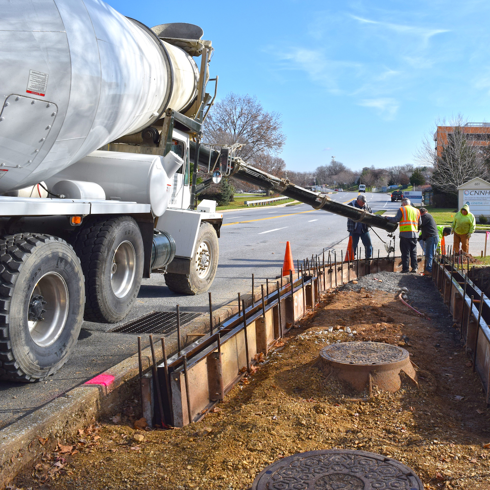 Three men and a cement vehicle doing construction by the roadside