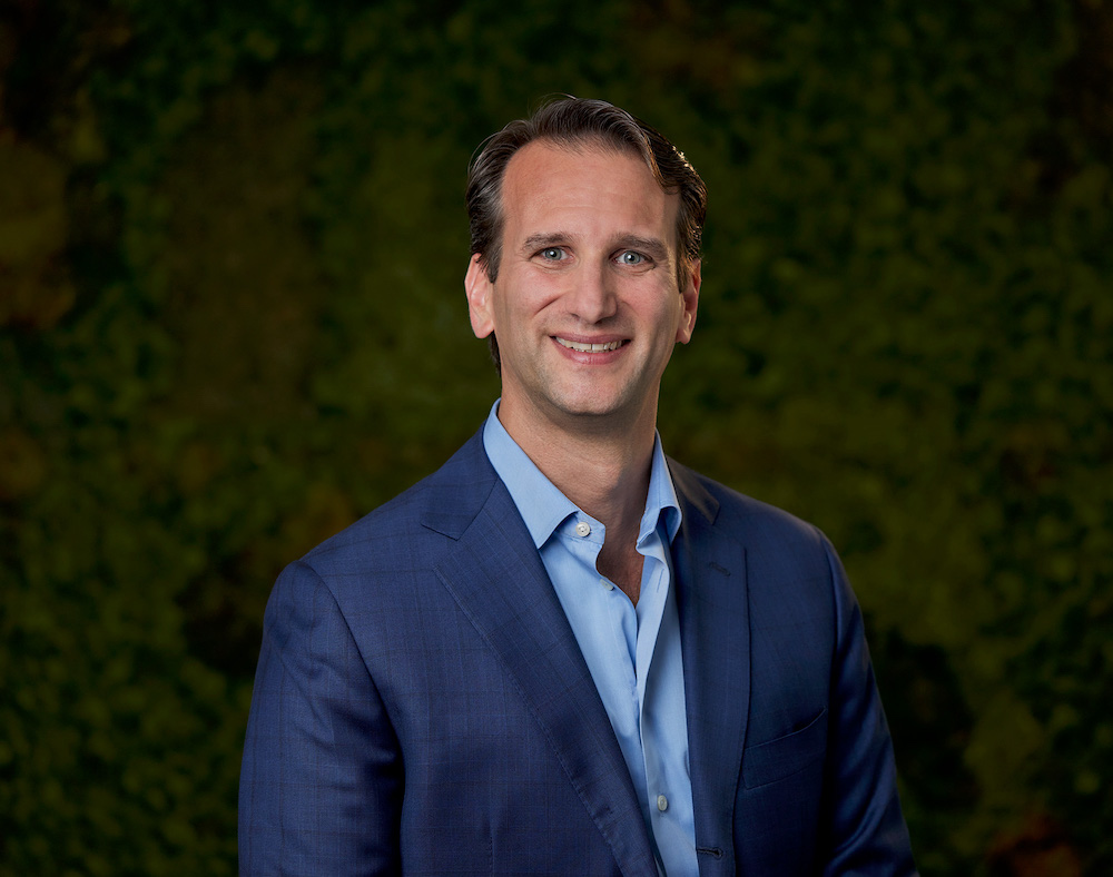 personin blue blazer and dress shirt smiling in front of green background