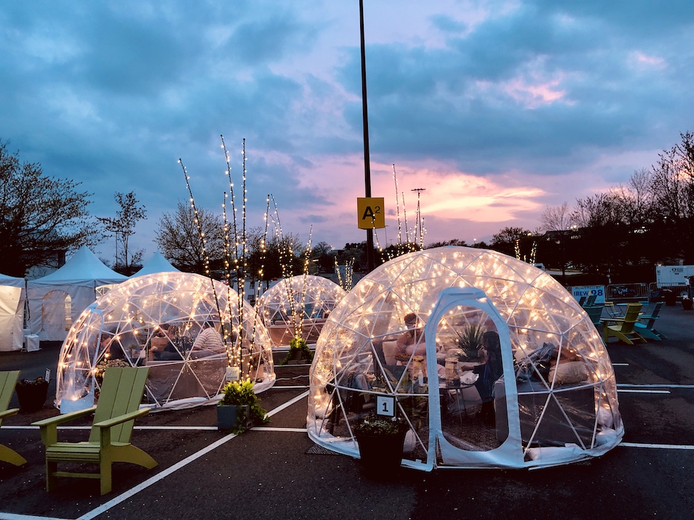 Four clear plastic garden/dining igloos outdoors with a sunset