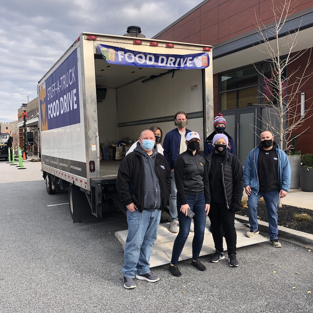 A box truck with "food drive" signs on it and seven masked individuals posing in front of it