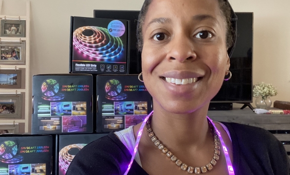 Person smiling with LED light strip over their shoulders and boxes of LED light strips in the background