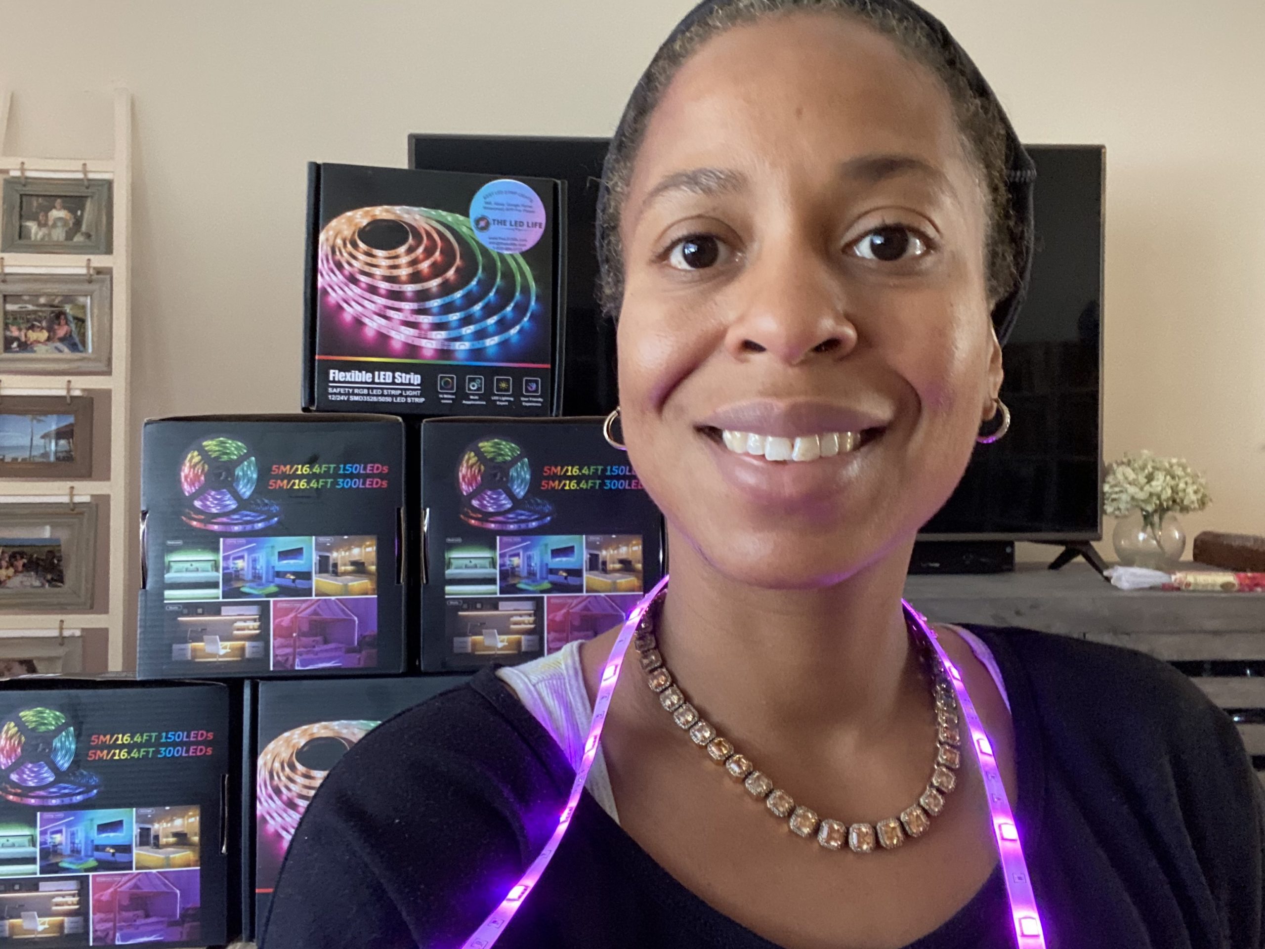 Person smiling with LED light strip over their shoulders and boxes of LED light strips in the background