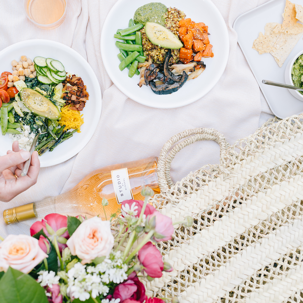 aerial view of plates of colorful food, a bottle of wine, a bag and flowers