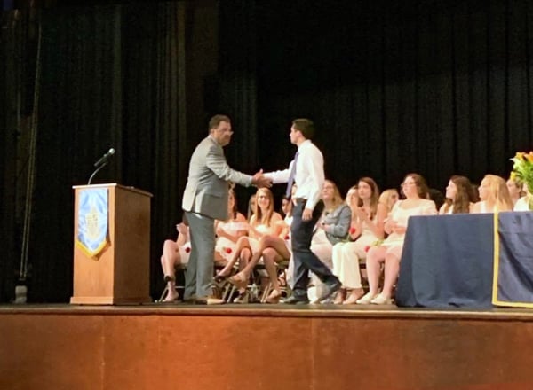 2 people shaking hands on a stage at a school event