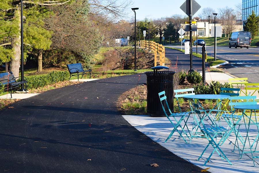 cement pathway with brightly colored tables and chairs, benches and a trash receptacle