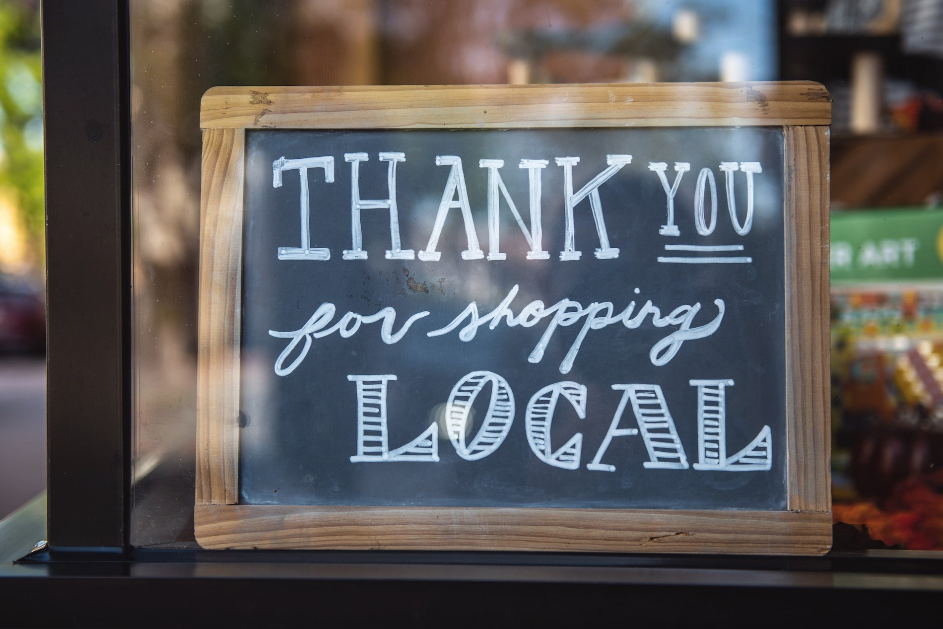 chalkboard sign in a window that says "Thank you for shopping local"