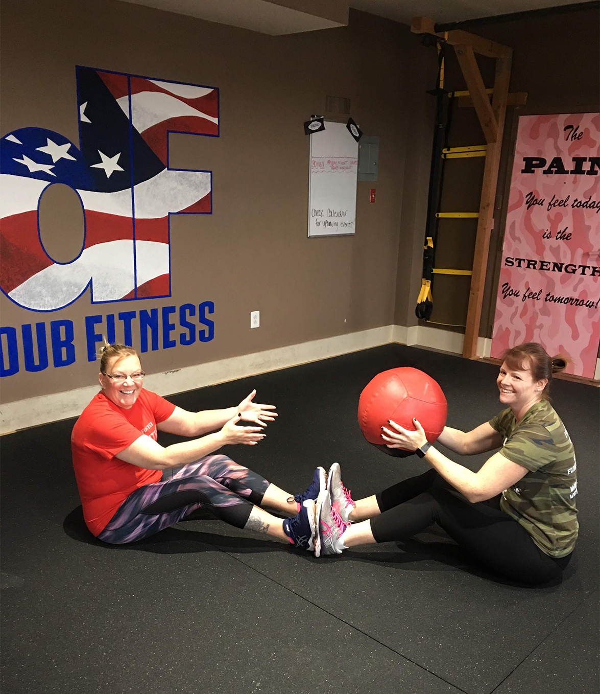 Two people sitting on the ground doing a medicine ball exercise