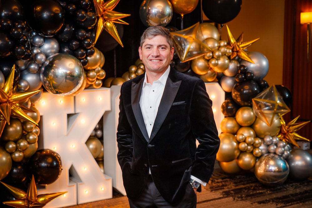 Person in velvet jacket standing in front of balloon and marquee backdrop