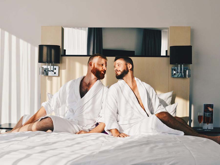 two people in robes on hotel bed looking at each other 