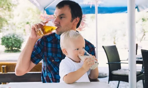 Man drinking a beer with a child on his lap