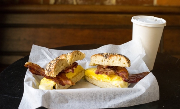 a bacon and egg bagel sandwich and a cup of coffee on a table
