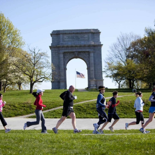group of people running gin front of large arch