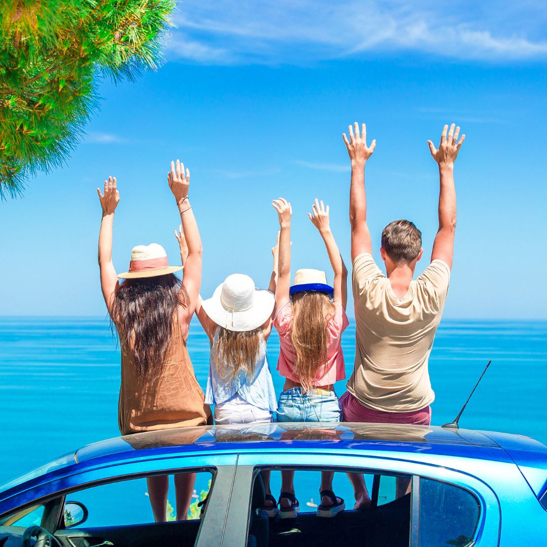 people sitting on top of a car with their handsin the air looking out at the ocean