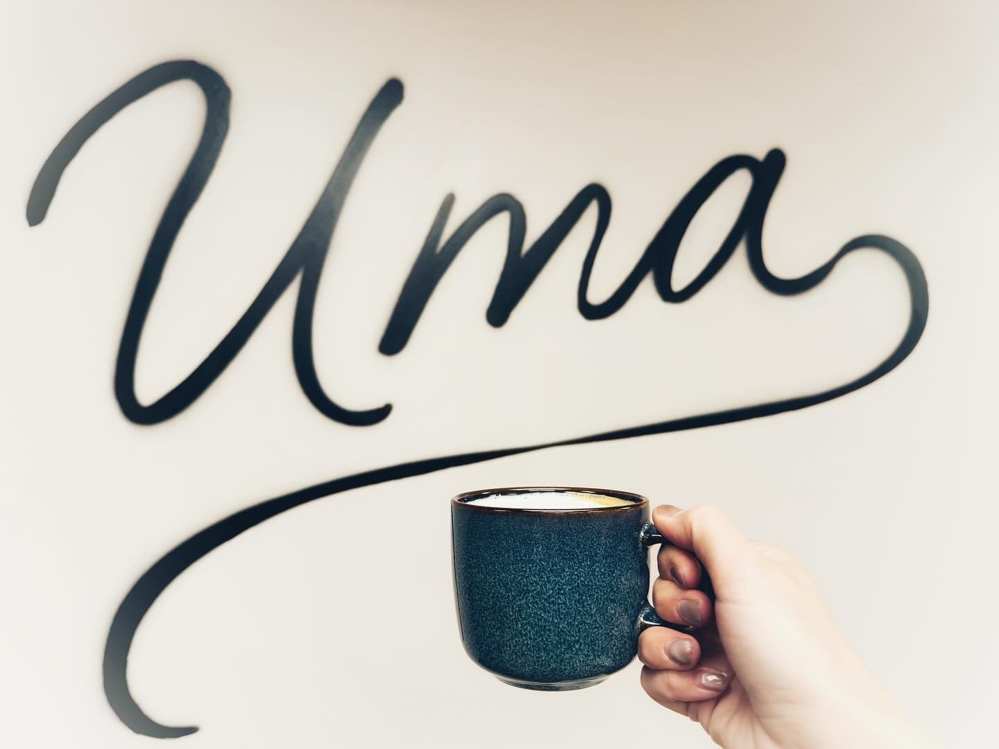 person holding coffee cup up in front of "Uma" sign