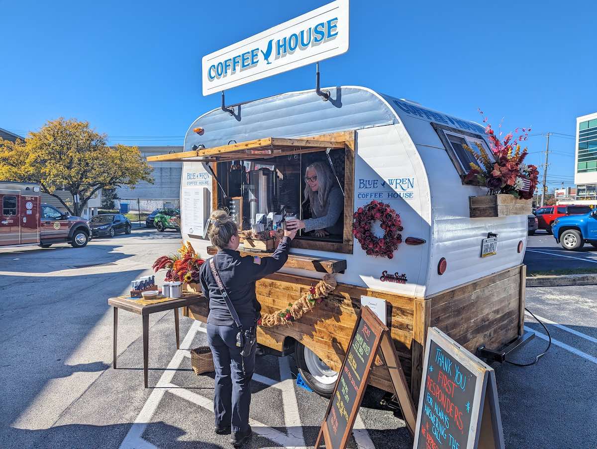 person handing coffee to a police officer out of an outdoor food truck