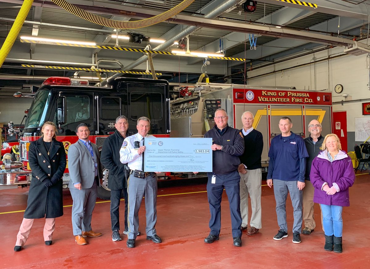 group of people standing in front of a fire truck holding a large check