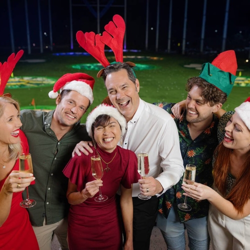 group of people in holiday attire smiling in front of a Topgolf bay