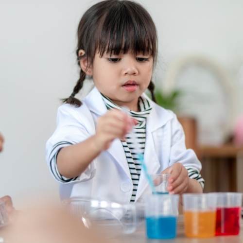 child in lab coat putting something into a beaker