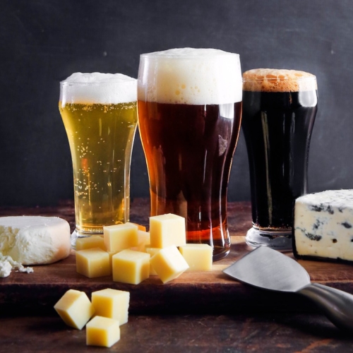 glasses of beer behind a cutting board of cheese