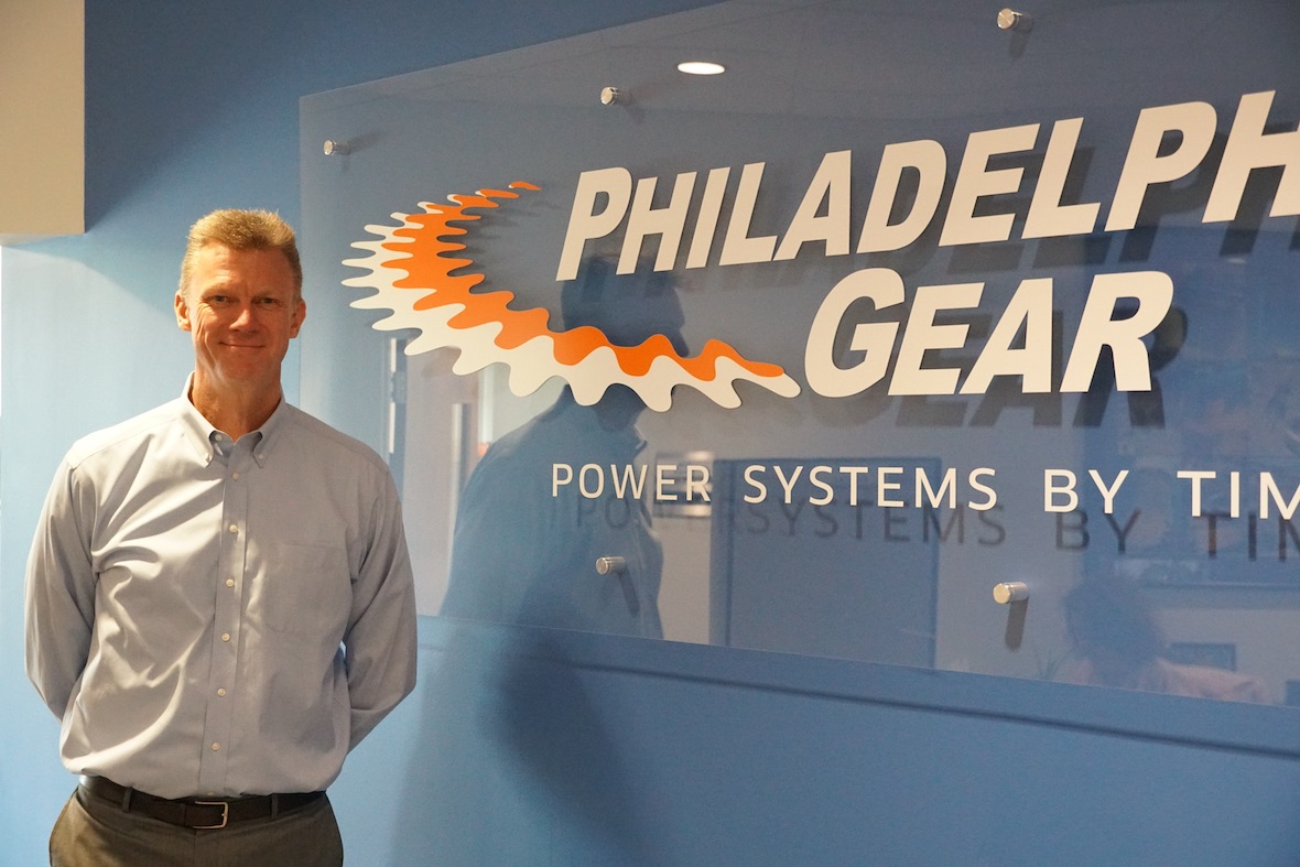 Carl Rapp standing in front of large Philadelphia Gear logo