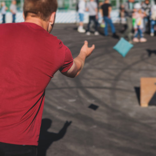 person throwing a cornhole bag in a parking lot