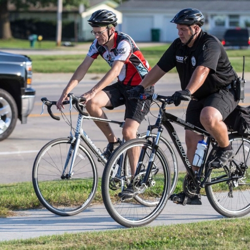 a police officer and a person in bike riding gear riding bicycles along a pathway
