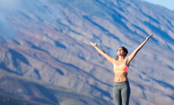 Person standing outdoors by a mountain with their arms in the air