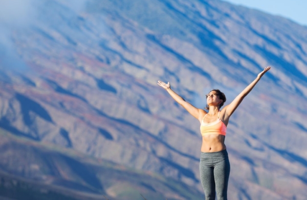 Person standing outdoors by a mountain with their arms in the air