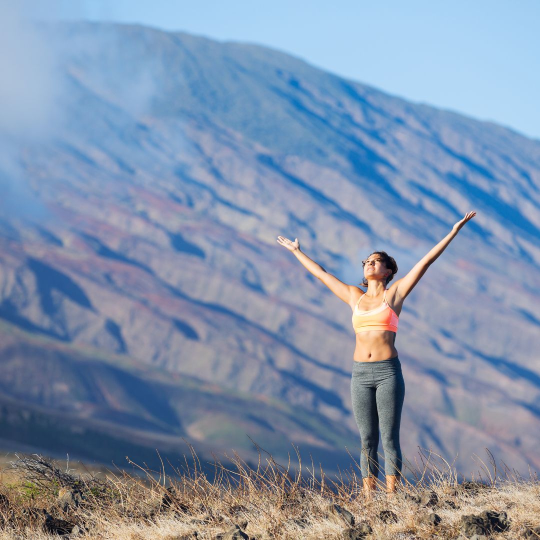 Person standing outdoors by a mountain with their arms in the air