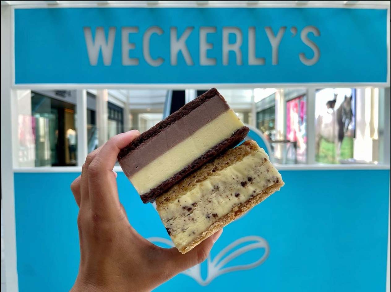 hand holding an ice cream sandwich in front of a Weckerlys sign