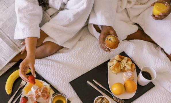 two people in white robes with trays of breakfast in a bed