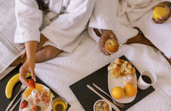 two people in white robes with trays of breakfast in a bed