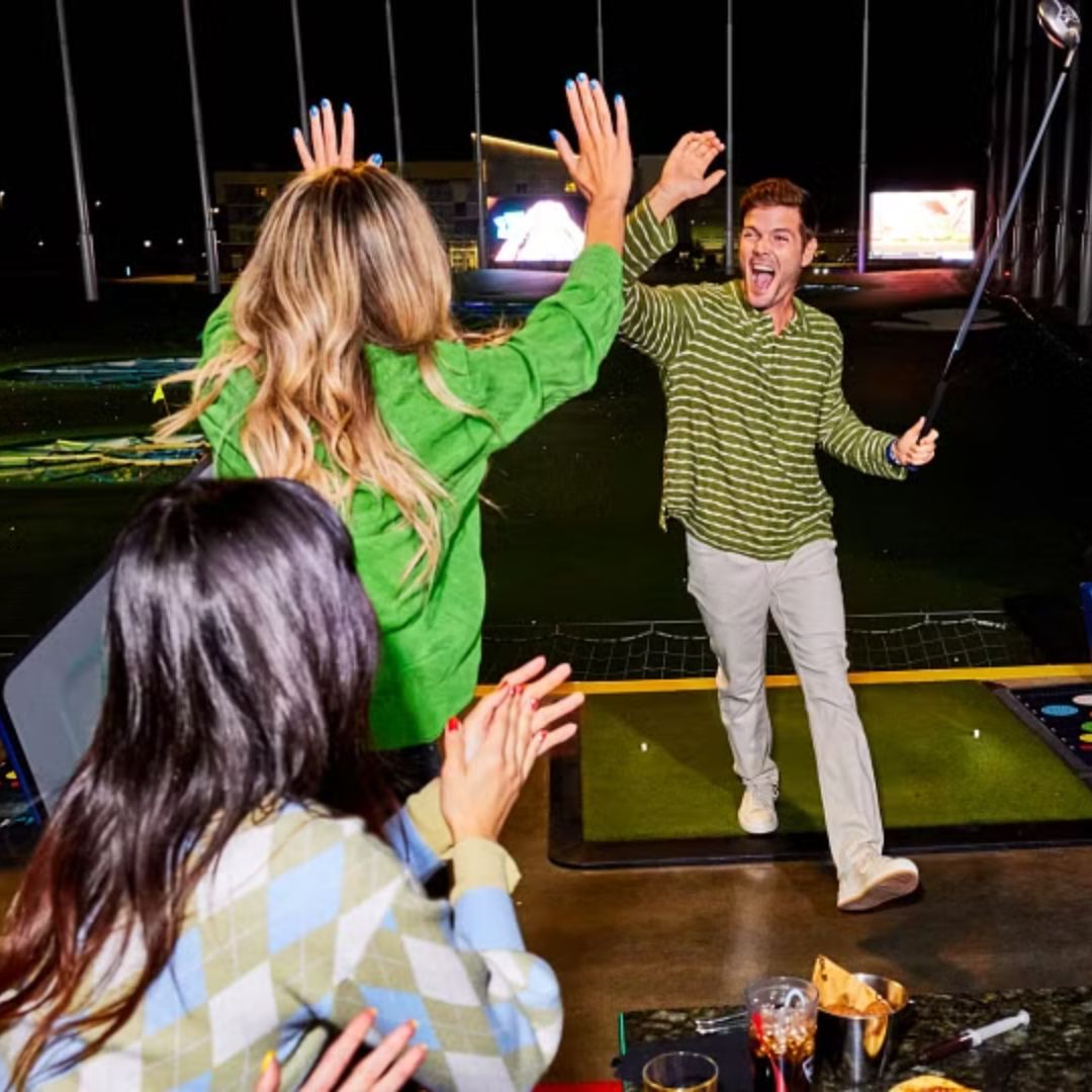 two peope high fiving at night in a golfing facility bay