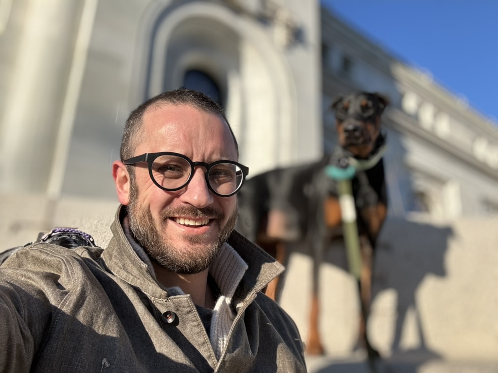 man sitting on steps outdoors with dog in background