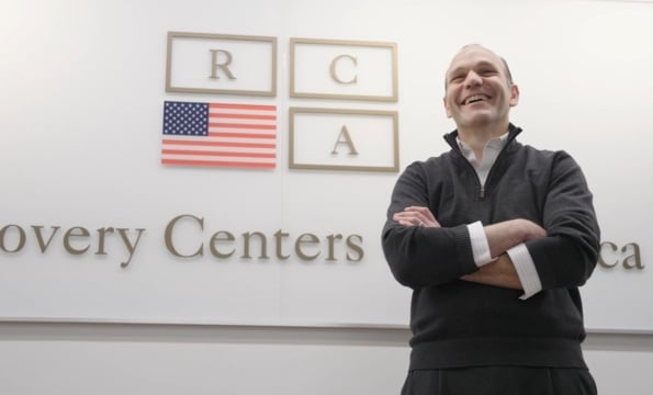 Brett Cohen smiling in front of a wall with Recovery Centers of America logo on it
