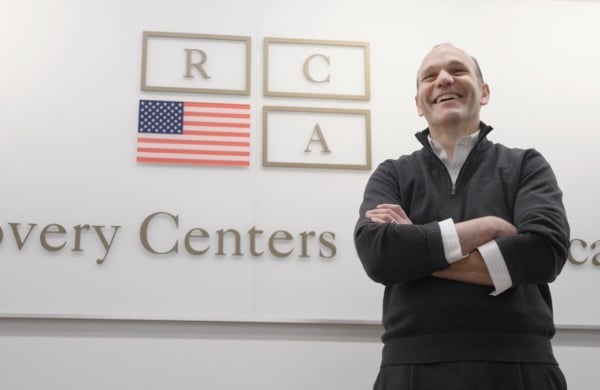 Brett Cohen smiling in front of a wall with Recovery Centers of America logo on it
