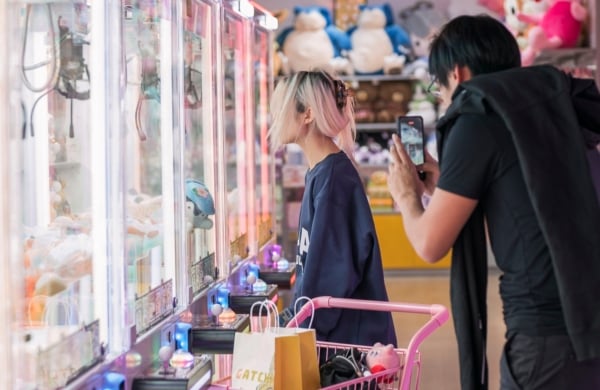 person standing outside of a gatchapon while another person takes a cellphone photo