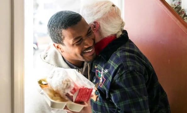 person hugging another person in a doorway, hodling a takeout meal