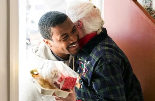 person hugging another person in a doorway, hodling a takeout meal
