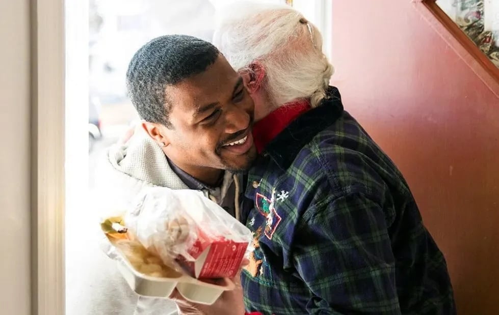 person hugging another person in a doorway, hodling a takeout meal