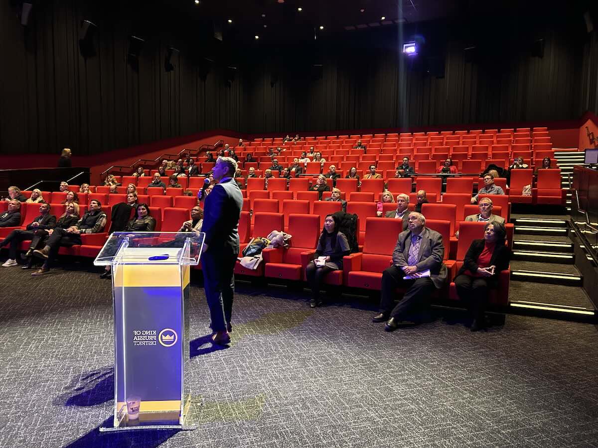 person at podium with crowd in theater seating in background